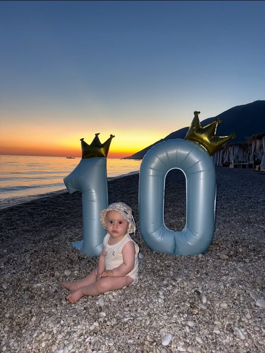 Maren dhjetë muajsh në plazh me tullumbacet 10 në perëndim